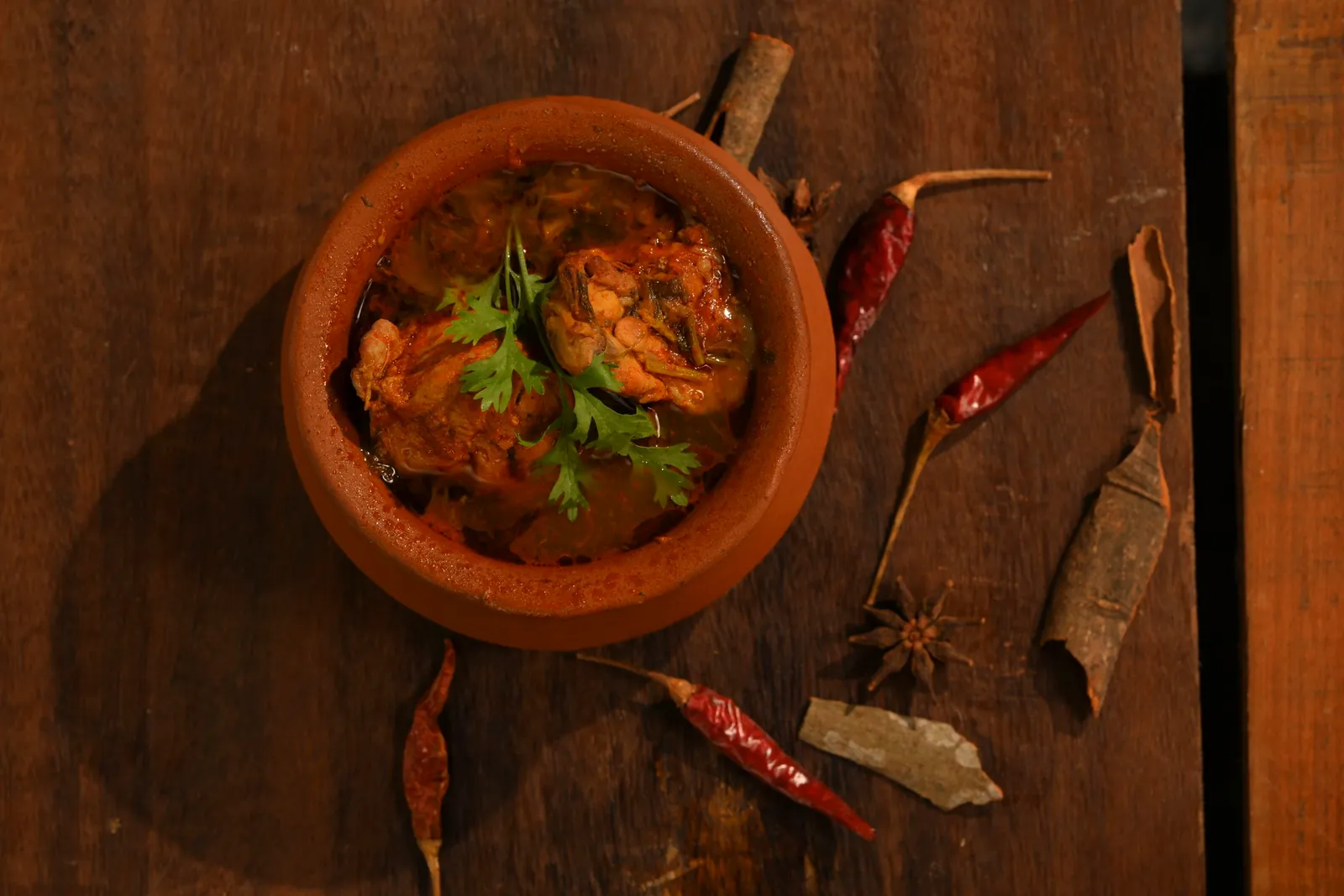 A curry in a clay pot with whole spices